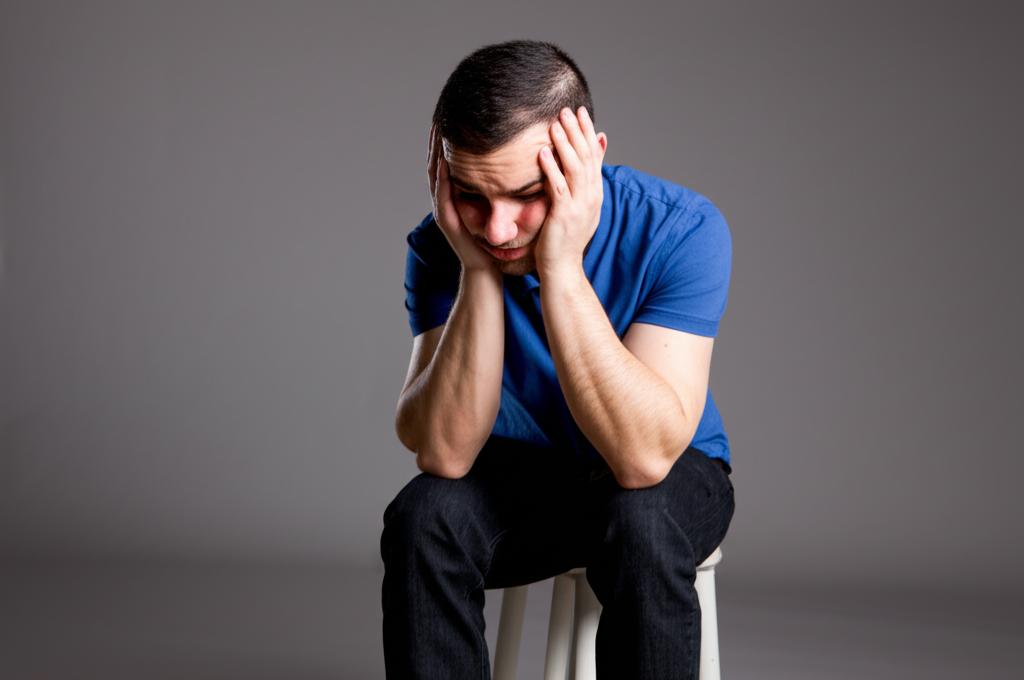 Worried man sitting alone, looking down, feeling inadequate