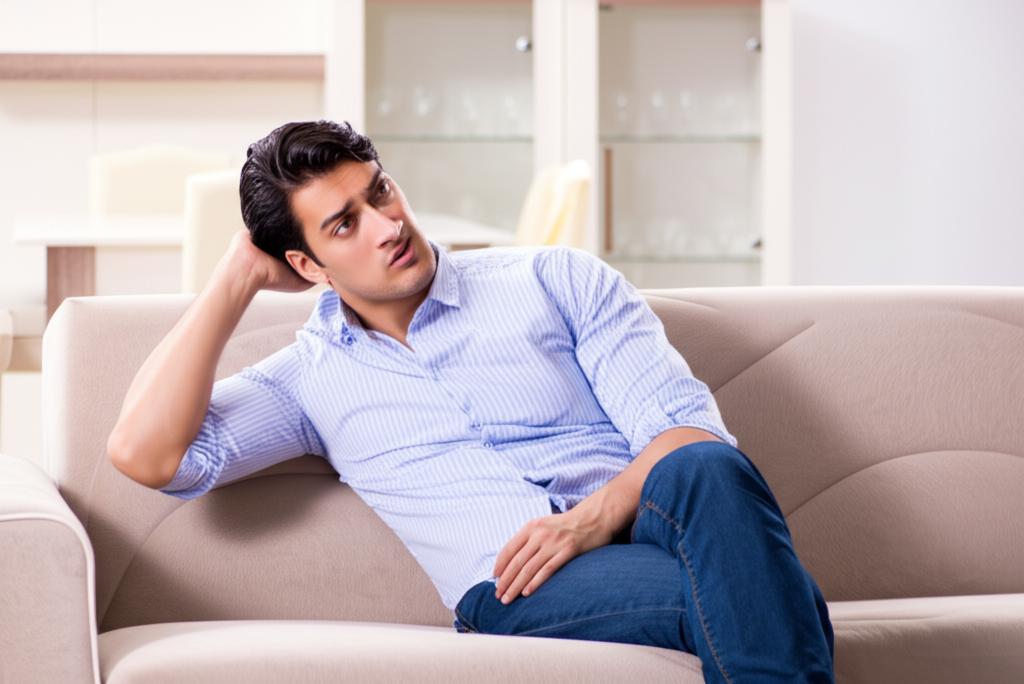 A man looking thoughtful and slightly stressed, sitting on a sofa, representing the problem of decreased intimacy.
