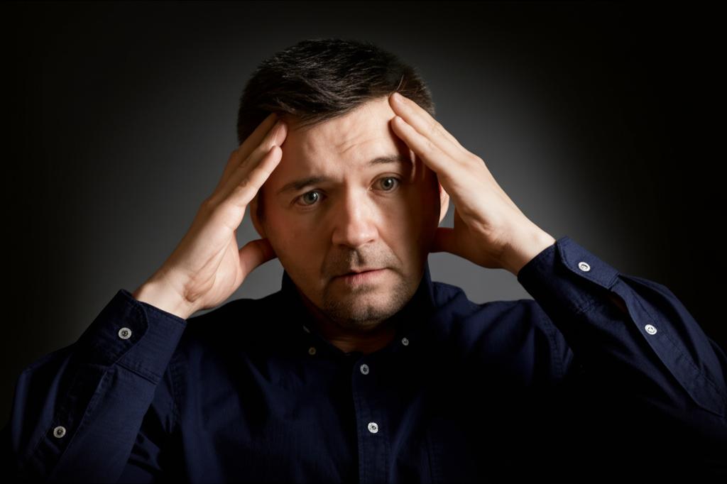 Man looking stressed, holding head, dark colors, symbolic of pressure affecting vitality