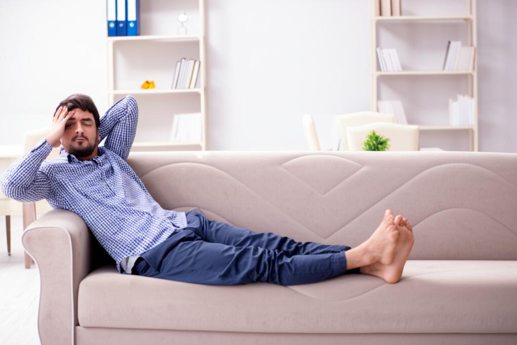 A tired man lying on the sofa, looking exhausted and unmotivated.