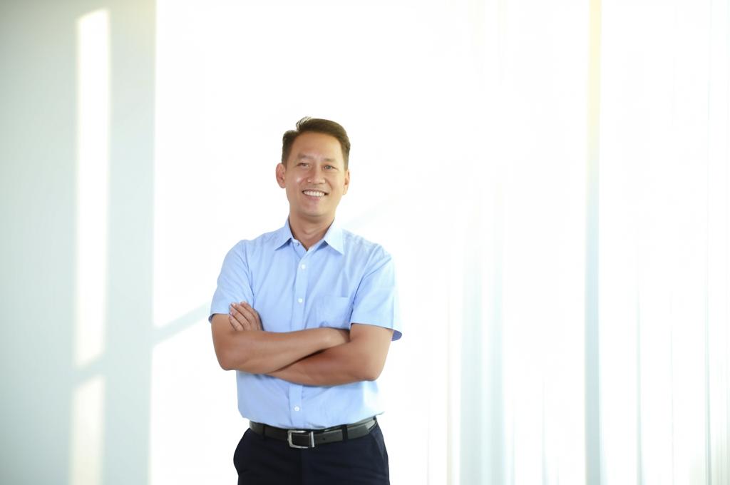 a middle-aged asian man smiling confidently, standing upright, sunlight streaming in, representing vitality and improvement, realistic photo