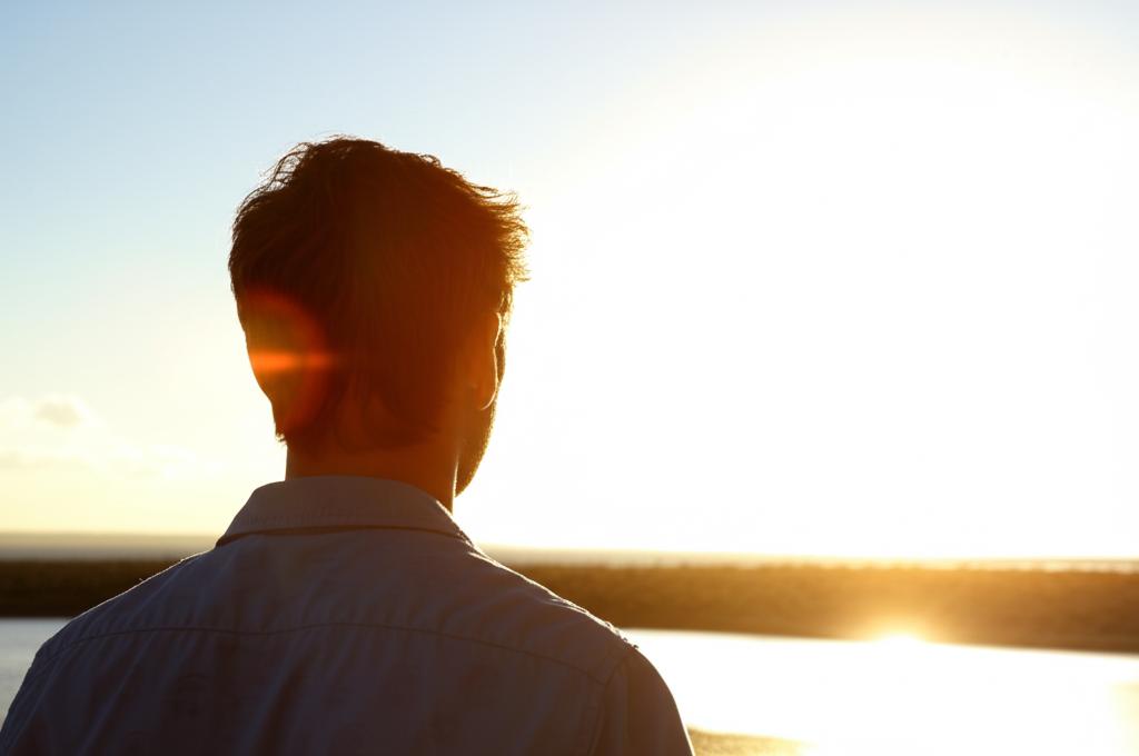 A man looking confidently towards the horizon, symbolizing renewed hope and self-esteem after overcoming challenges. AI art, bright sunlight, positive atmosphere.
