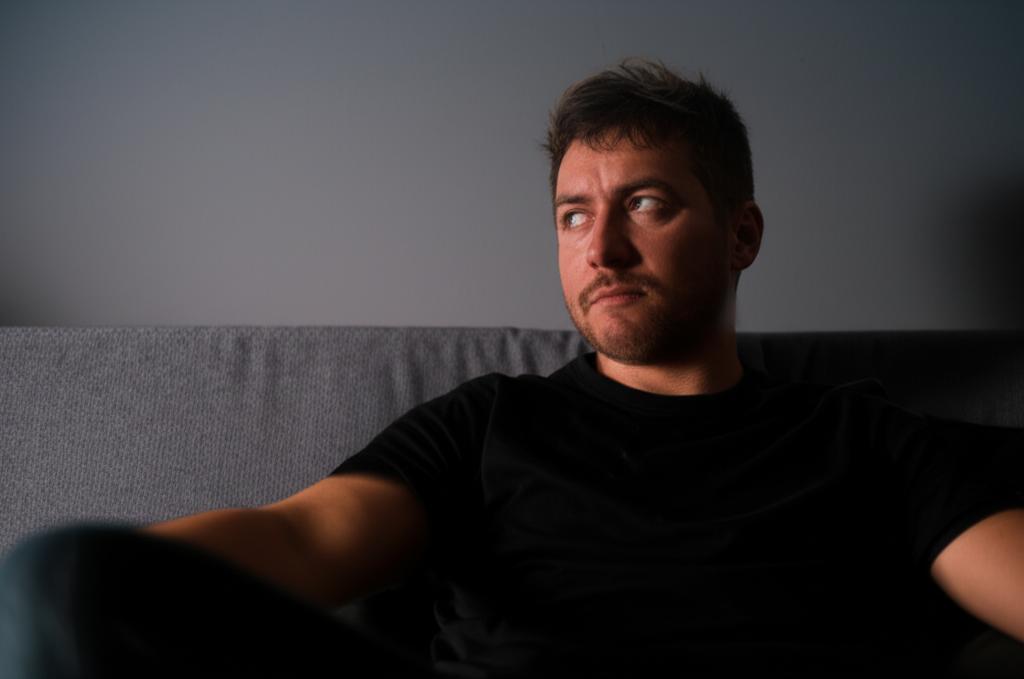 man sitting on sofa looking tired after intimacy, low energy, dim light